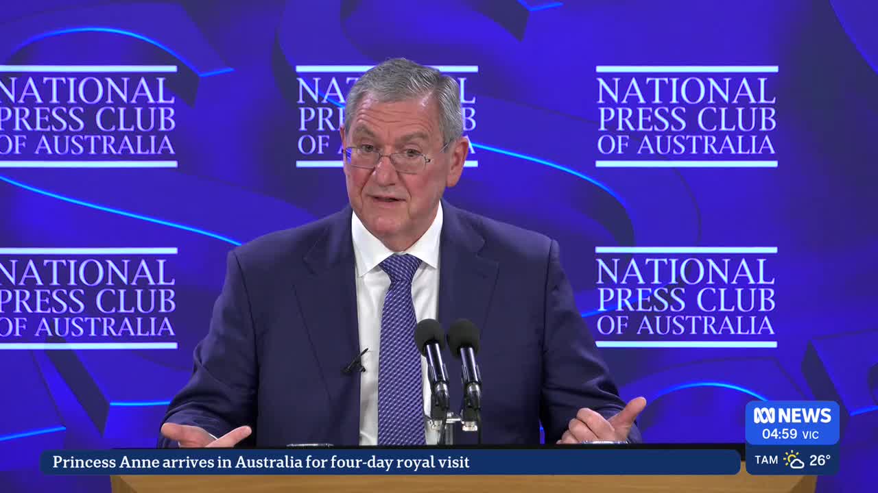 A man in a suit speaks into microphones at the National Press Club of Australia. ABC News is broadcasting the event, with a headline about Princess Anne's vi...