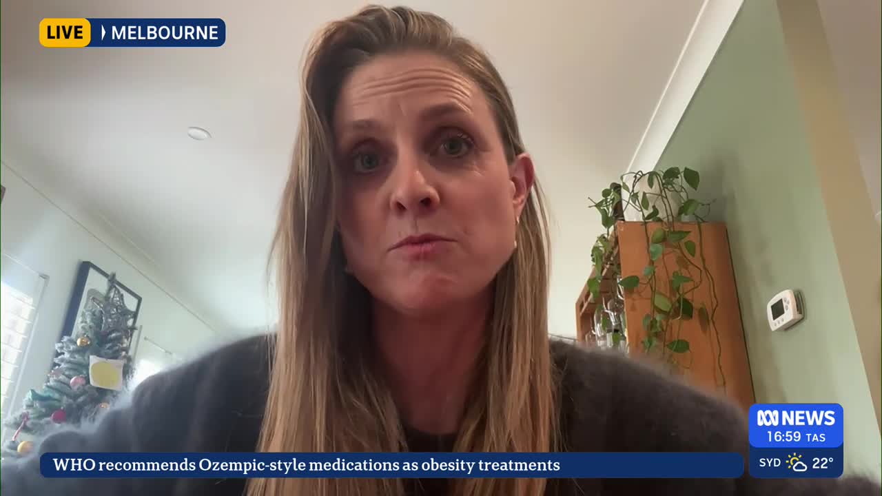 A woman with long blonde hair is speaking directly into the camera, likely for ABC News in Australia. Behind her, a small Christmas tree and some potted plan...