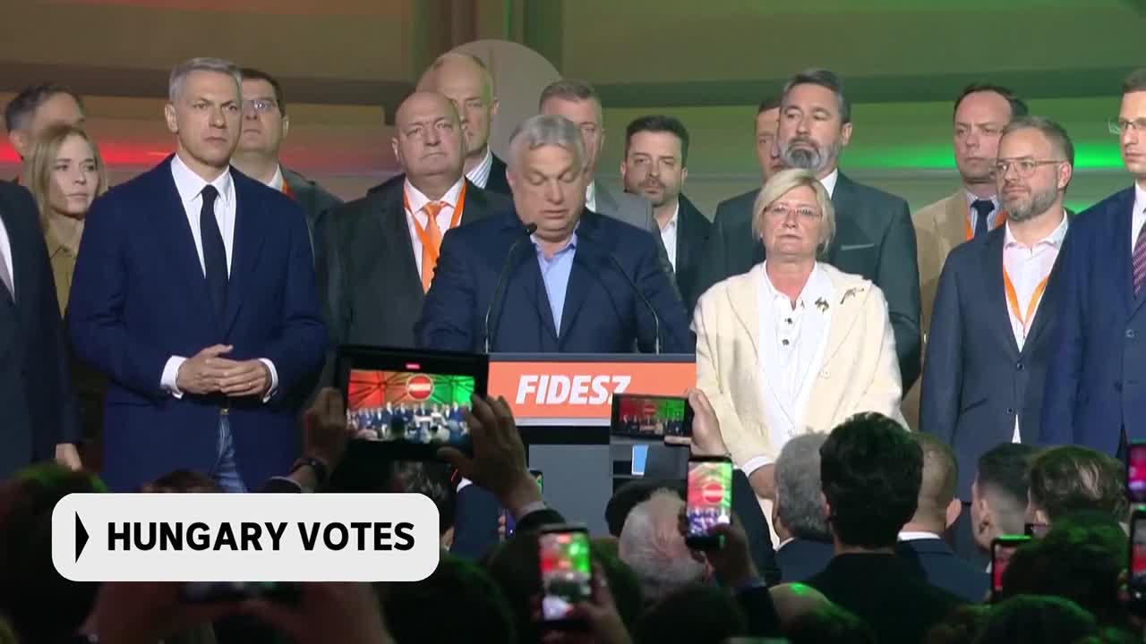The man at the podium, Viktor Orbán, speaks to a crowd as supporters hold up phones to record. A banner behind him reads "FIDESZ," the name of his political ...