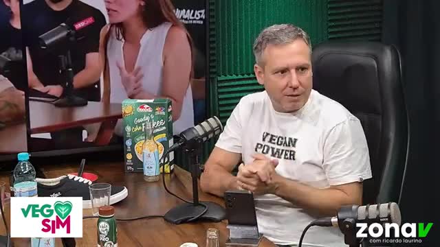 The man in the "Vegan Power" t-shirt is leaning forward, hands clasped, as if in conversation. On the table in front of him, a box of cereal and a bottle of ...