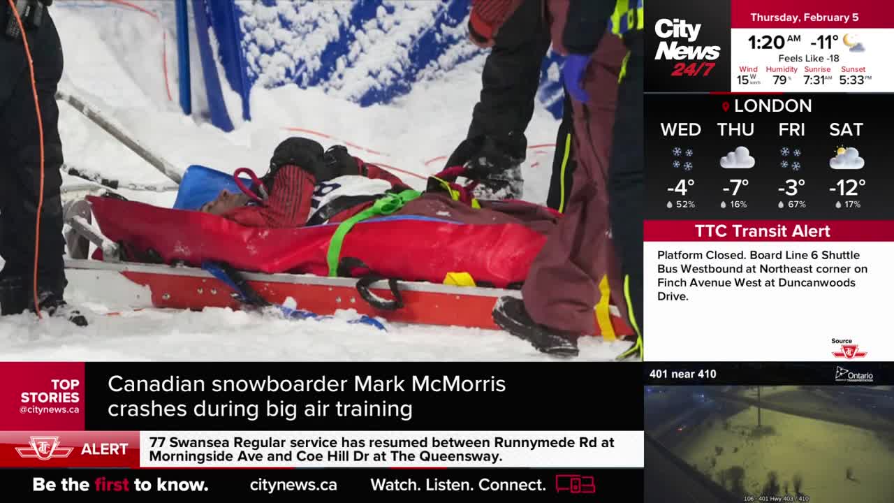 Paramedics are carefully lifting a snowboarder on a red stretcher through the snow. The Canadian athlete appears to be injured after a big air training session.