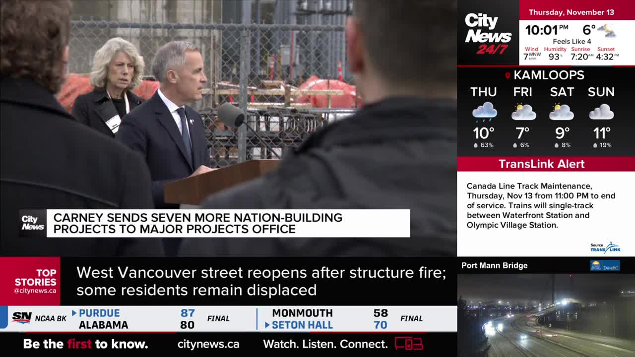 A man in a suit speaks into a microphone, with a CityNews banner beneath him. Behind him, a woman stands quietly, and the background shows construction.