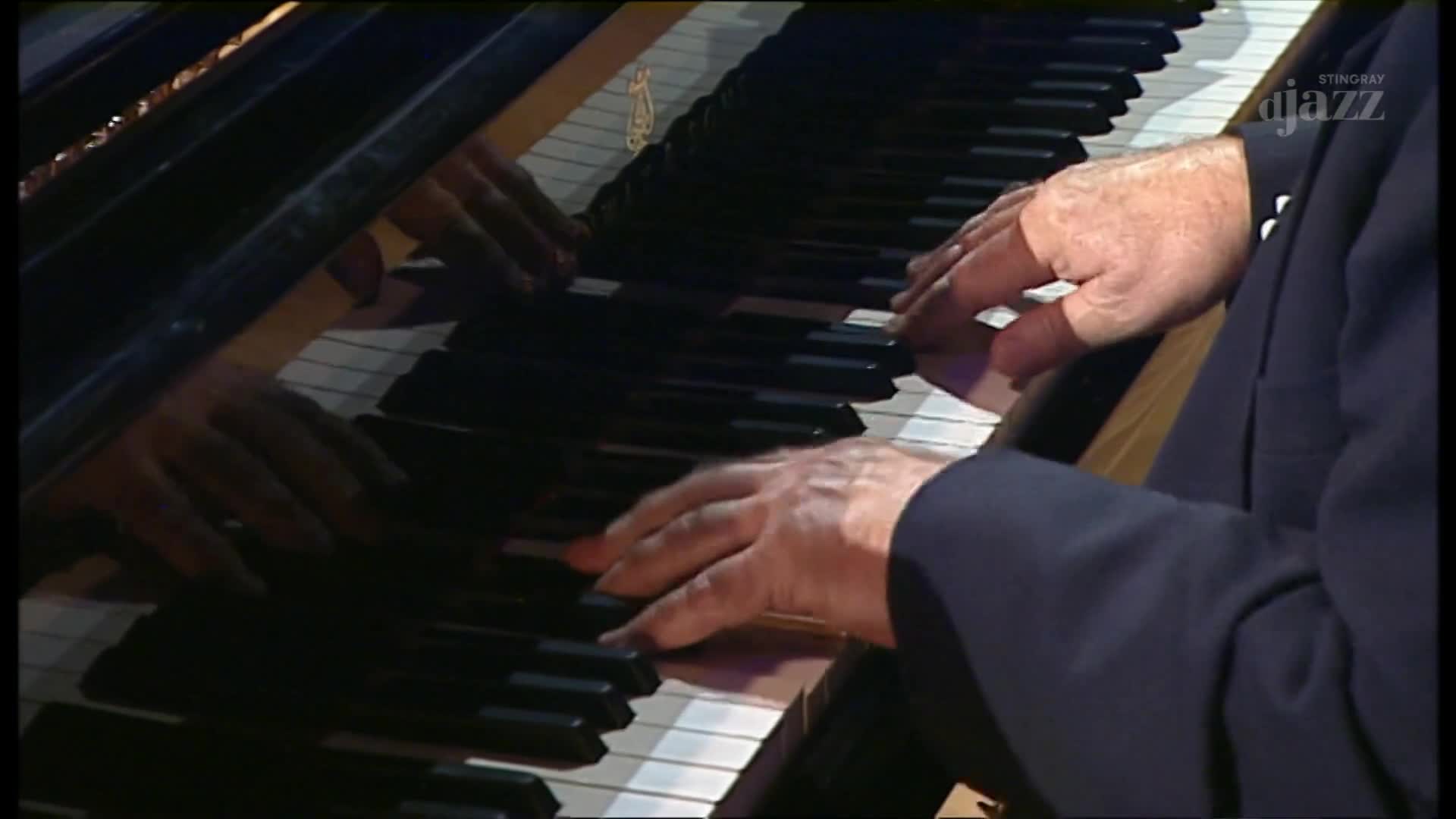 A pianist's hands dance across the keys, the polished surface reflecting his movements. The music, broadcast on Stingray DJAZZ from Canada, fills the space w...