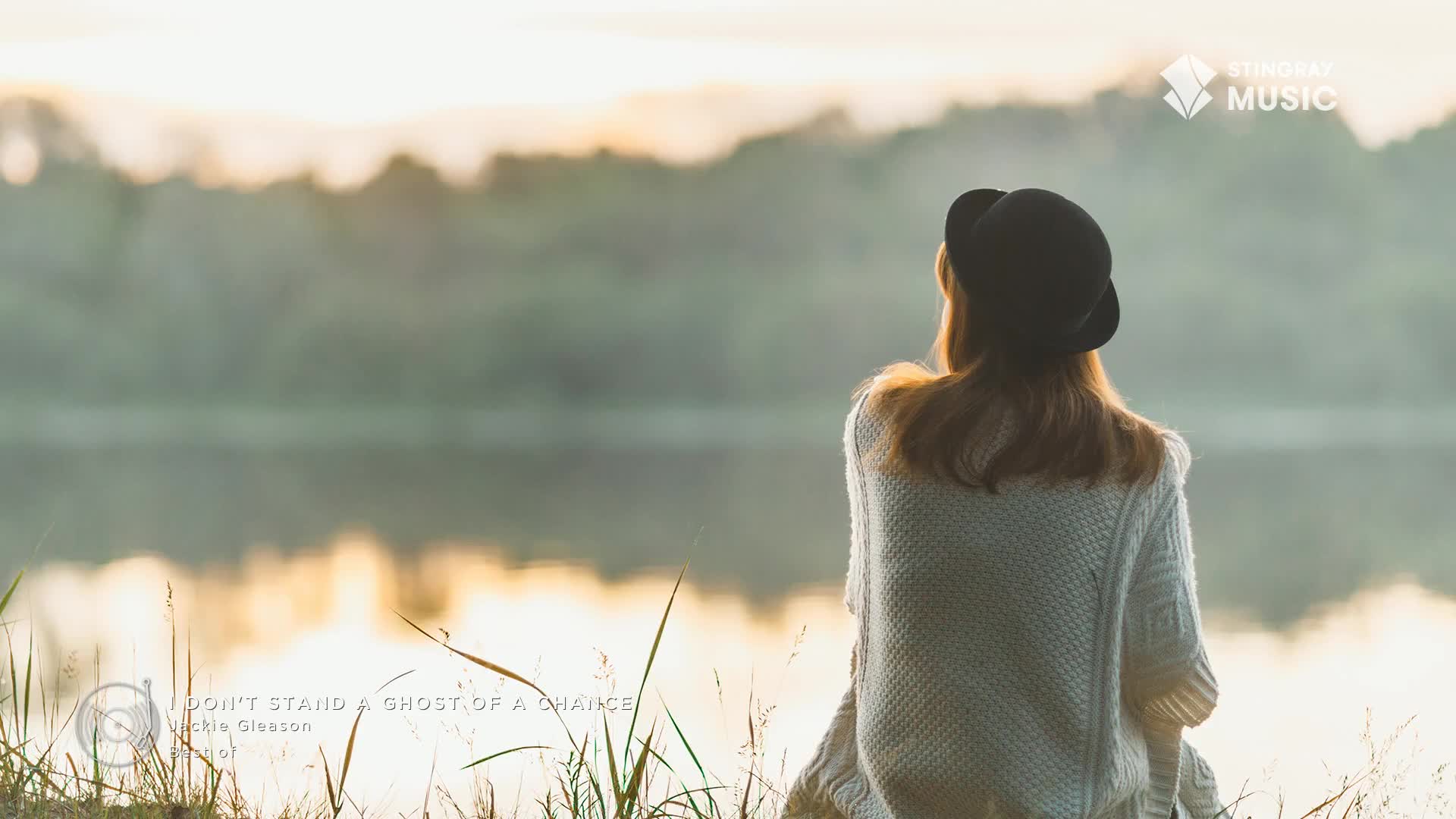 A woman in a black hat sits by the water, gazing at the serene landscape. The Stingray Easy Listening logo sits in the corner, and the song playing is "I Don...