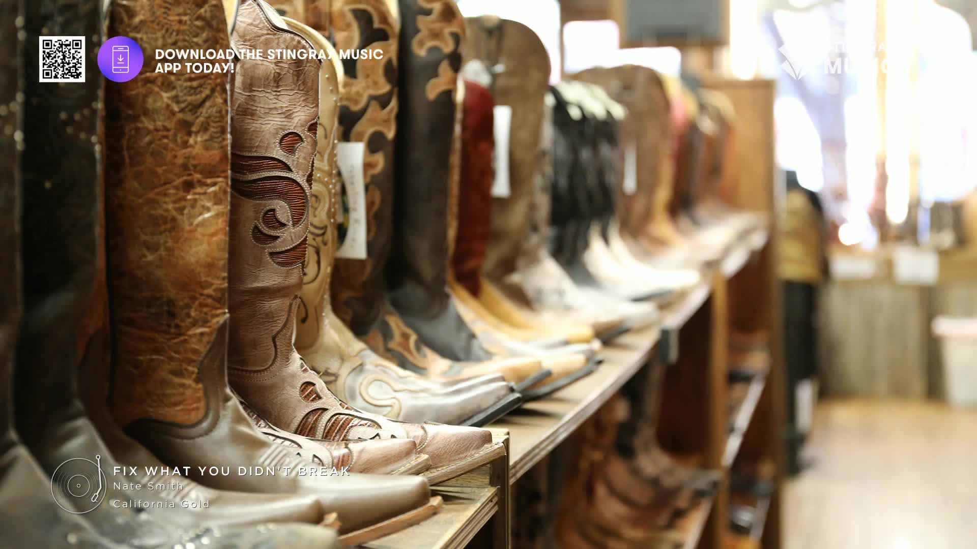 Boots of various styles and colors stand shoulder-to-shoulder on a wooden shelf. The Stingray Hot Country logo and a song title are visible at the bottom, hi...