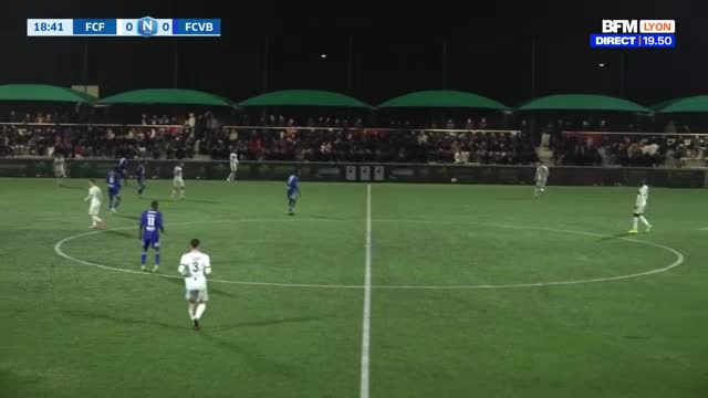 A football match is underway, the score tied at 0-0. Players in white and blue jerseys move across the green pitch under the stadium lights. Spectators fill ...