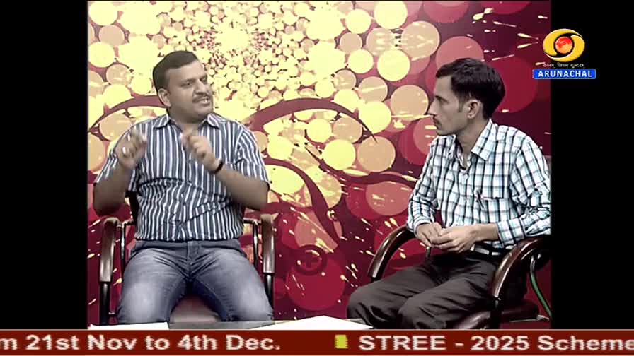 On the DD Arun Prabha set, a man in a striped shirt gestures animatedly while speaking. His companion, in a checkered shirt, listens intently.