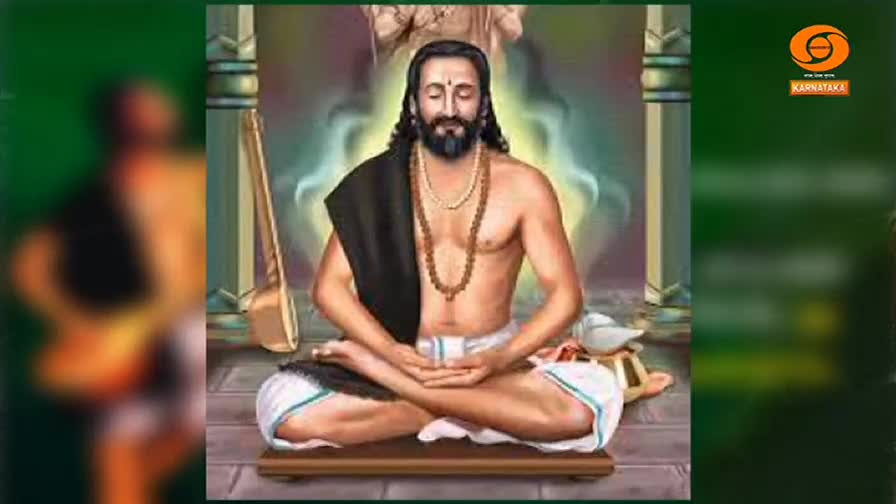A man with a long beard sits in meditation, his hands resting gently in his lap. A tanpura leans against a pillar, and the DD Chandana logo is visible in the...