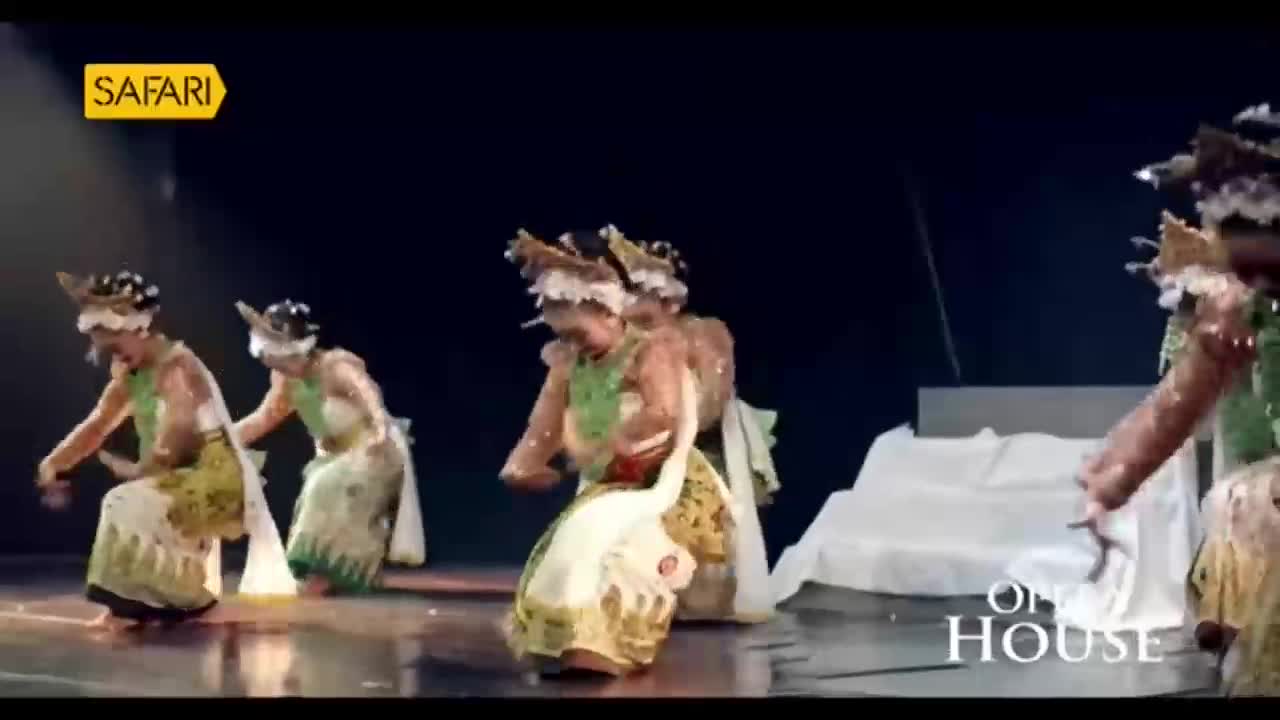 Dancers in elaborate headdresses and long, patterned skirts move across the stage, their arms gracefully extended. The performance, likely from India and bro...