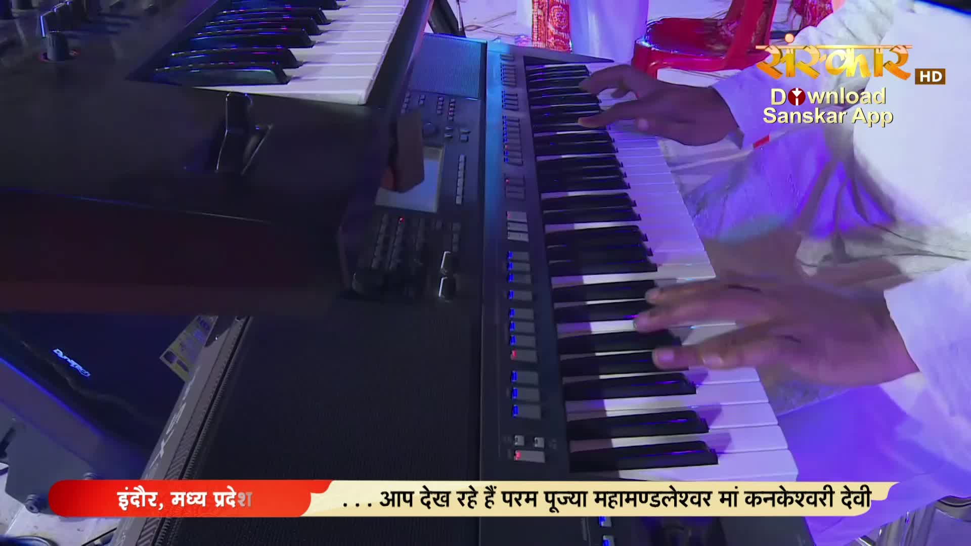 Fingers dance across the keys of a synthesizer, the white and black keys reflecting the stage lights. The broadcast from Sanskar TV in India is underway.
