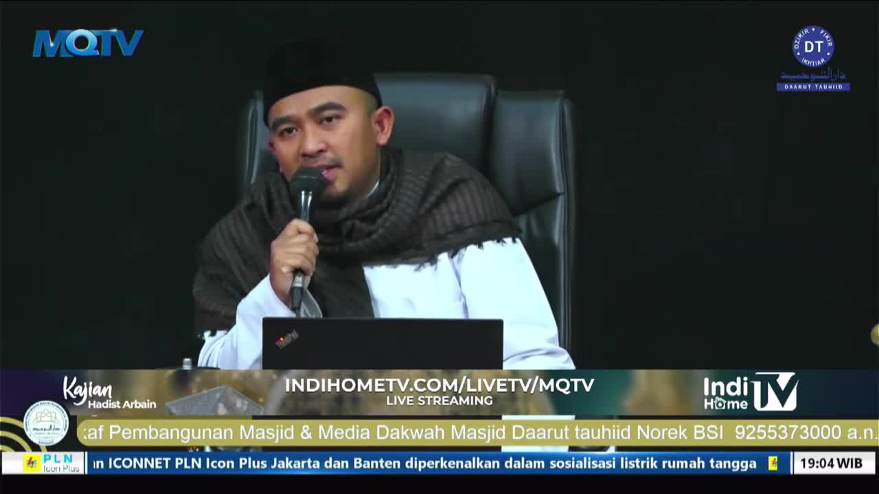 A man in a black cap and scarf speaks into a microphone, seated in front of a laptop. The MQTV logo is visible in the corner, and the broadcast is live strea...