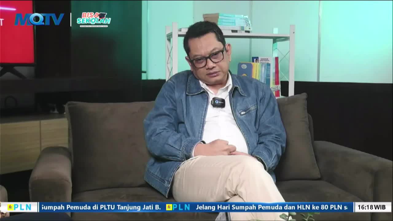 A man in a denim jacket sits on a couch, facing the camera on what appears to be an MQTV set. The Indonesian PLN logo and text are displayed at the bottom of...