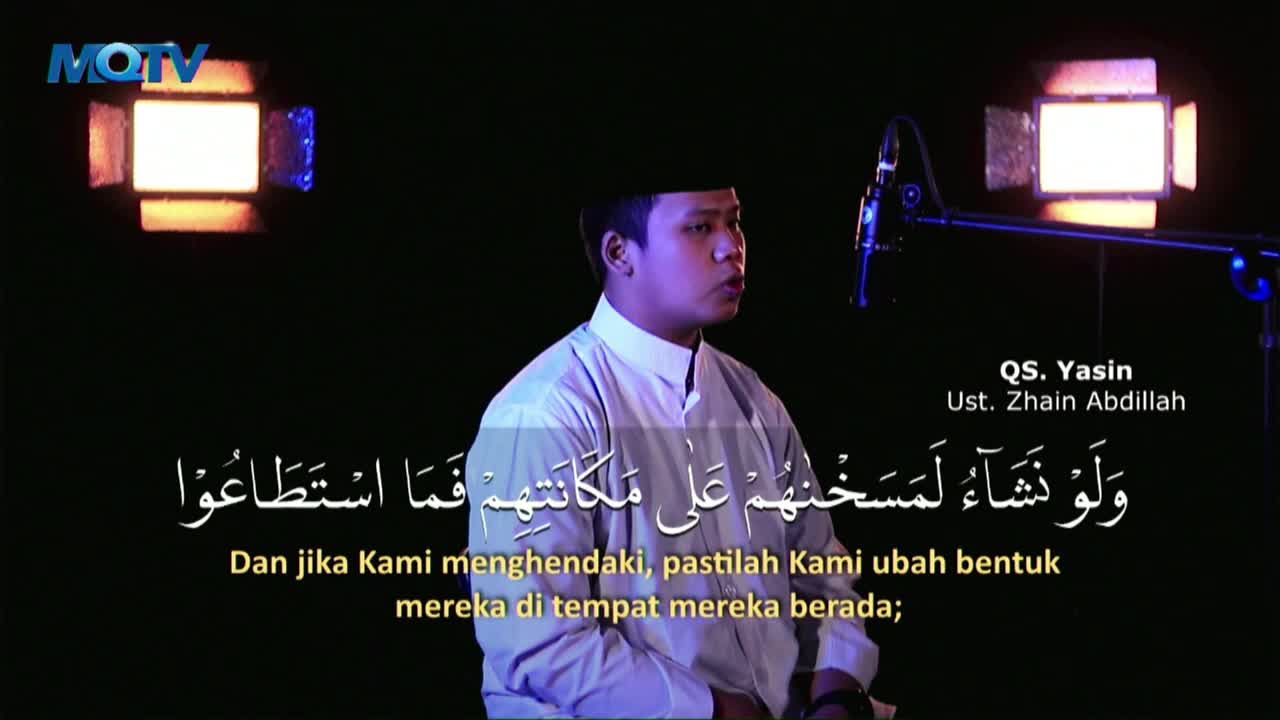 A man in a white shirt and black cap speaks into a microphone, his face illuminated by studio lights. Below him, Arabic script and its Indonesian translation...