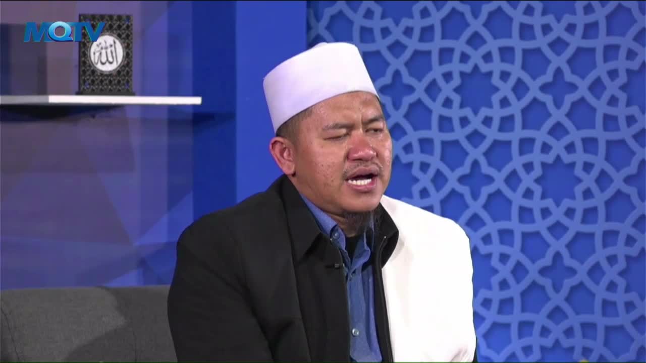 The man, wearing a white cap, is speaking with conviction, his mouth open. He's on a set with a blue patterned backdrop, the MQTV logo visible in the corner.