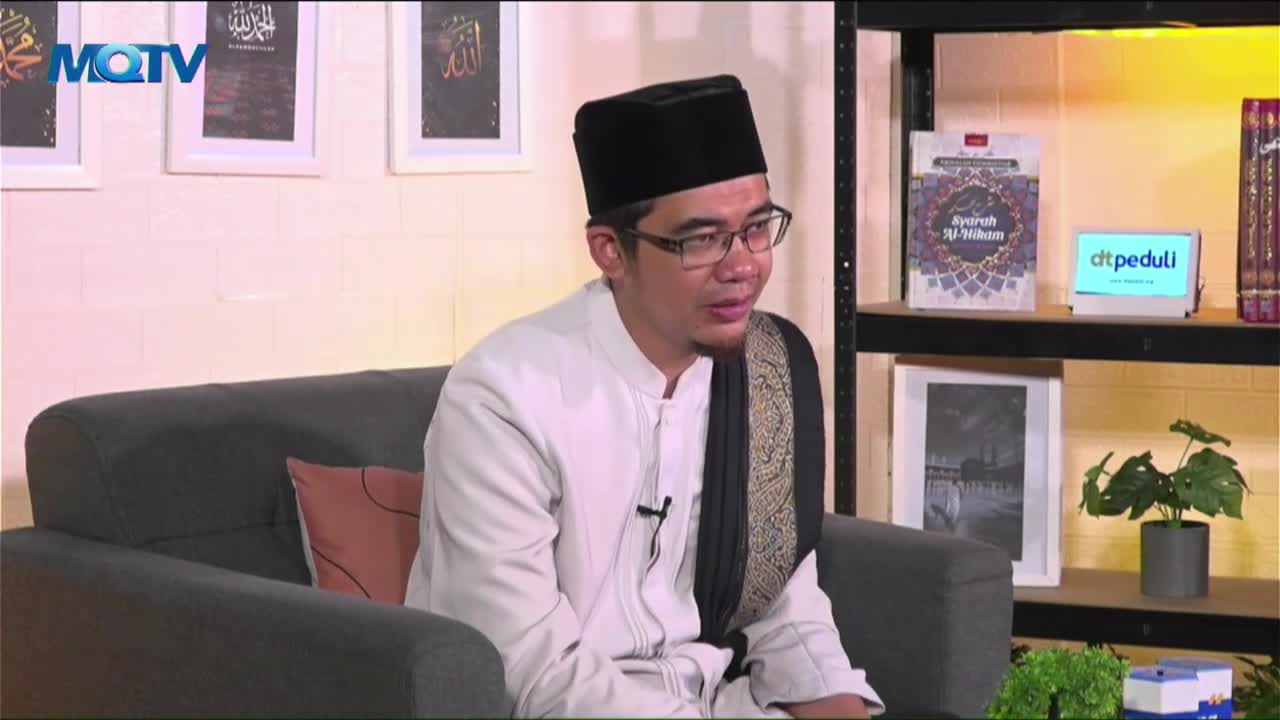 The man in the black cap and glasses is seated on a gray couch, speaking into the camera. Behind him, the MQTV logo is visible, and shelves hold books and a ...
