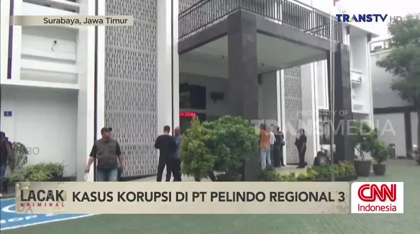 Outside a building in Surabaya, a group of people stand near the entrance, likely discussing the corruption case reported by Trans TV. The CNN Indonesia logo...