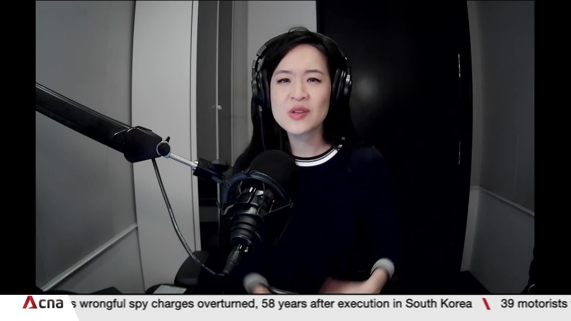 A woman with headphones speaks into a microphone, her face illuminated by the studio lights. The CNA International logo and breaking news crawl along the bot...