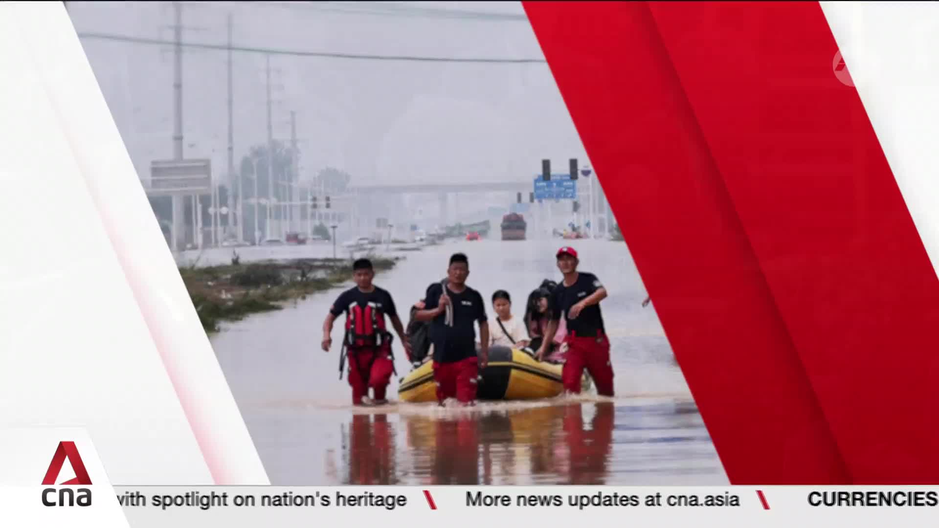 Volunteers, clad in red pants, wade through the flooded street, pulling a yellow raft with several people aboard. Overhead, the sky is overcast, and a bridge...
