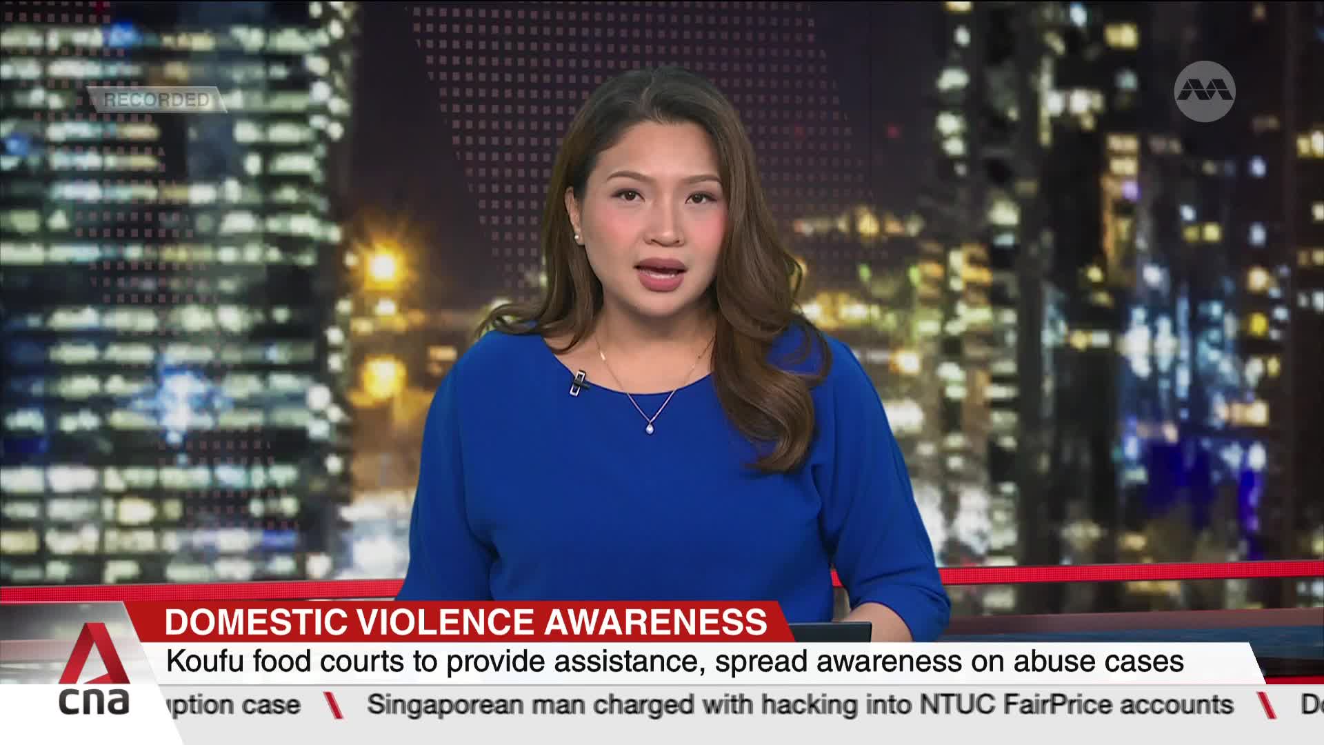 A woman in a blue blouse is speaking directly to the camera, framed against a backdrop of city lights. The CNA International logo is visible, and a news bann...