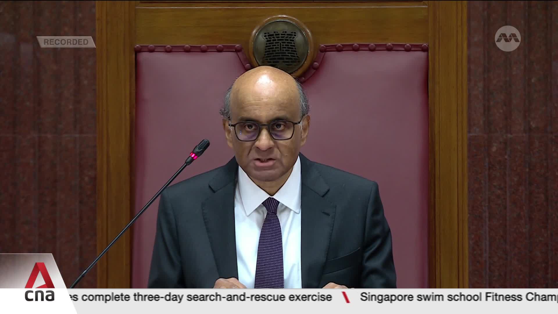A man in a suit, wearing glasses, speaks into a microphone. The CNA International logo is visible at the bottom of the screen, and the word "RECORDED" is in ...
