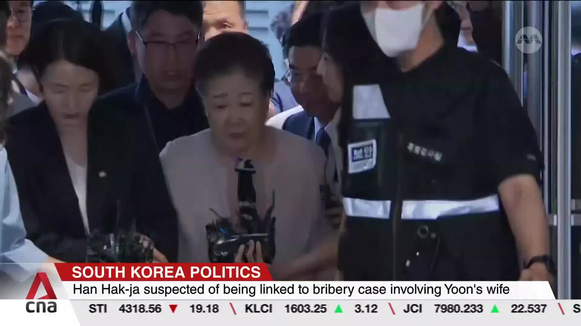 Amidst a throng of people, a woman is being escorted, her face etched with concern. The CNA International news ticker at the bottom provides context for the ...