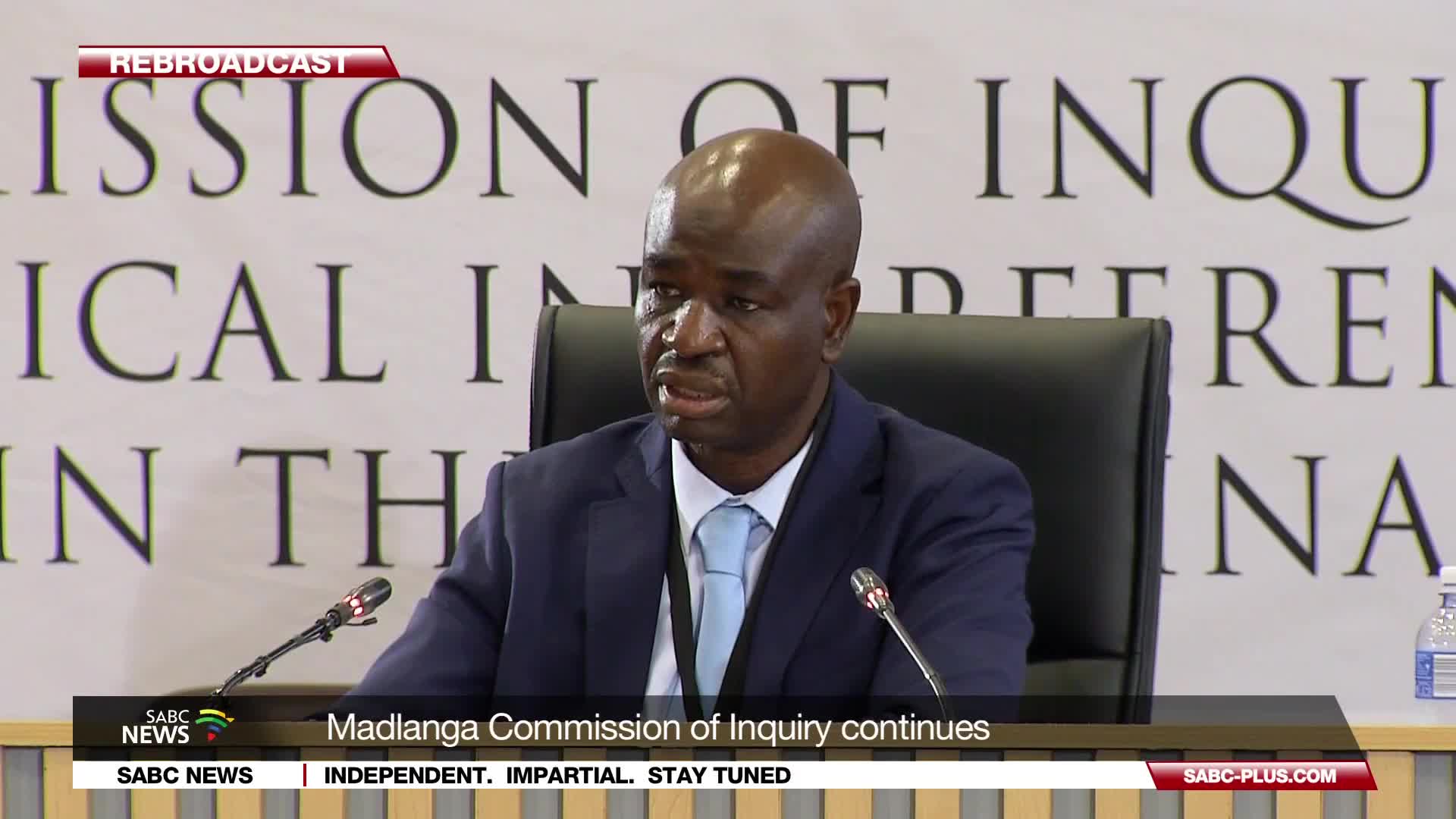 A man in a dark suit and light blue tie speaks into a microphone at a commission hearing. The SABC News banner at the bottom indicates the Madlanga Commissio...