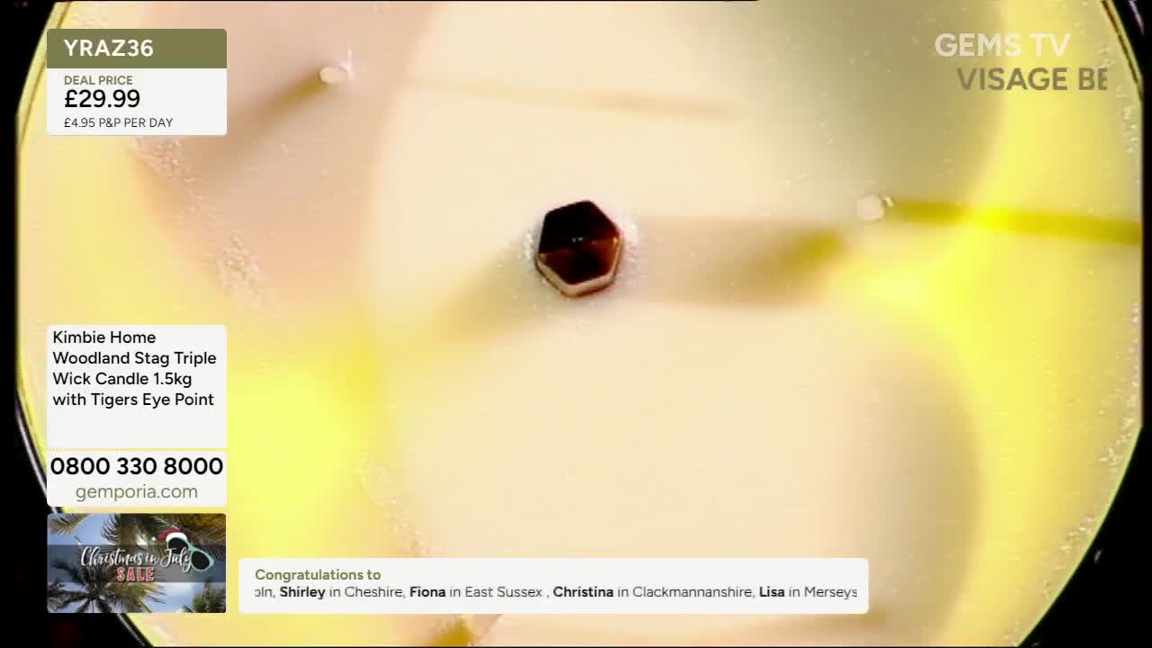A close-up of a candle is on display, with a dark, hexagonal stone embedded in the wax. The Gems TV logo is visible, along with details about the product and...