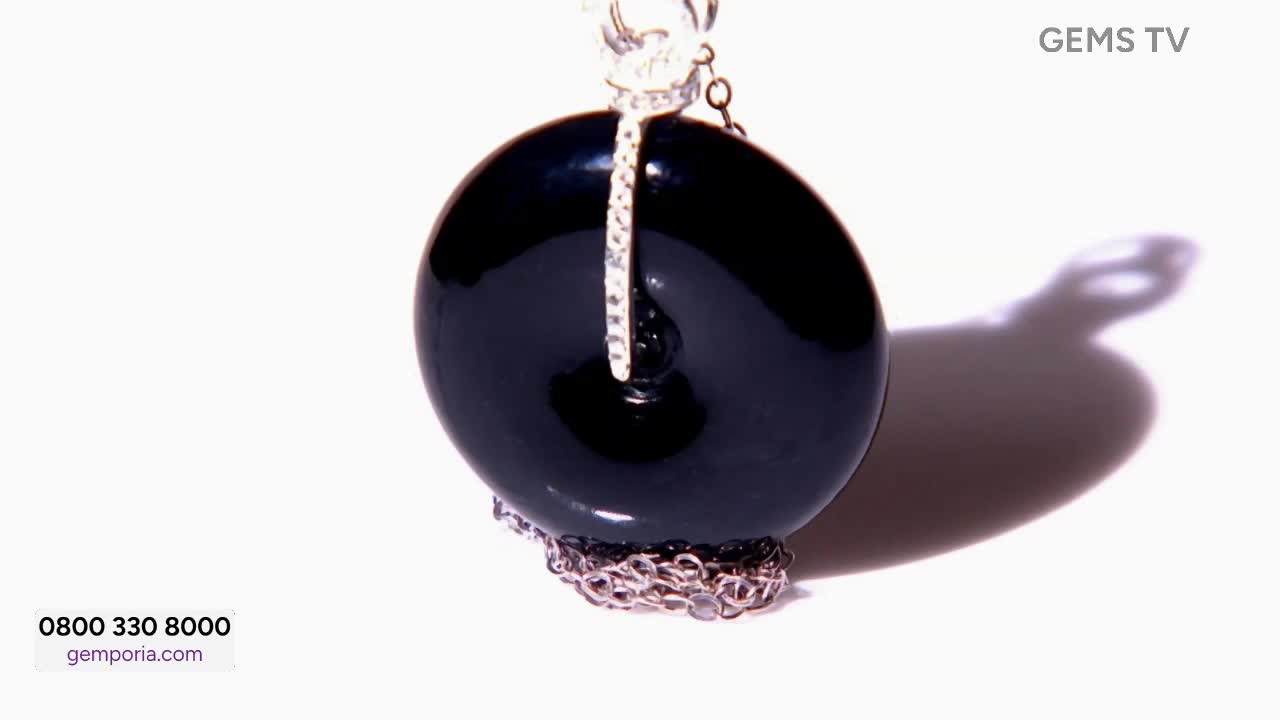 On Gems TV, a large, glossy black pendant hangs suspended against a bright white background. A silver chain and a diamond-studded bale support the round gems...