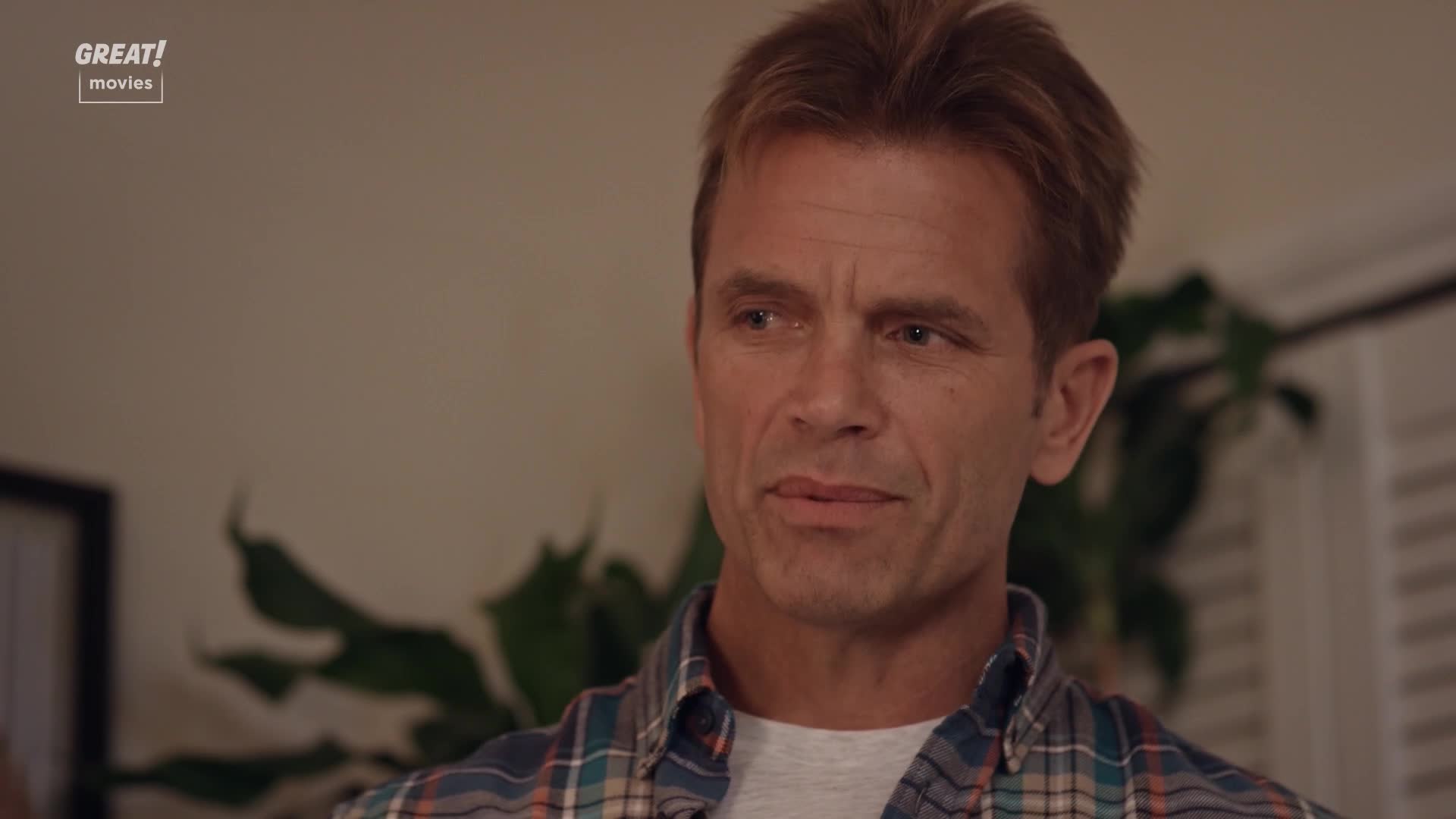 He's listening intently, his brow furrowed slightly as he considers something. The plaid shirt and the "GREAT! movies" logo suggest a cozy, made-for-TV film ...