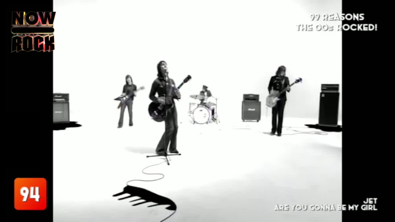 The band, framed by a stark white backdrop, is playing "Are You Gonna Be My Girl" on NOW Rock. The lead singer, with his guitar, is front and center, while t...