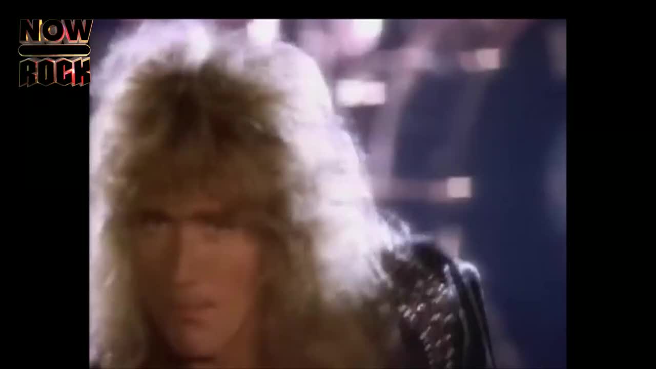 The singer's long, blonde hair is catching the light as he stares intently. His studded leather jacket glints, and he's ready to belt out a tune.