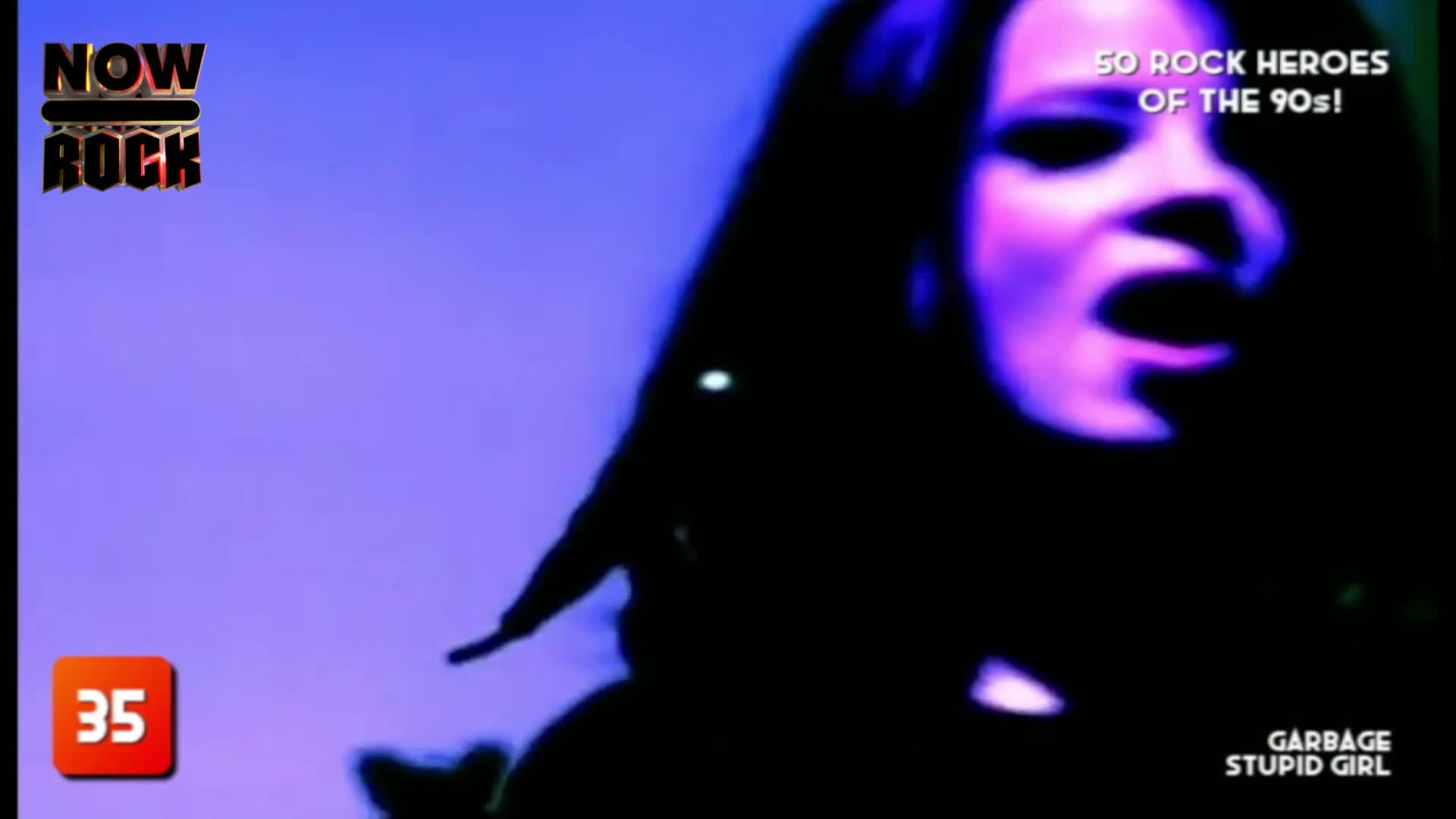 The singer's face is lit with purple, her mouth wide open as she belts out a song. Long, dark hair frames her face, and the background is a solid, cool-toned...