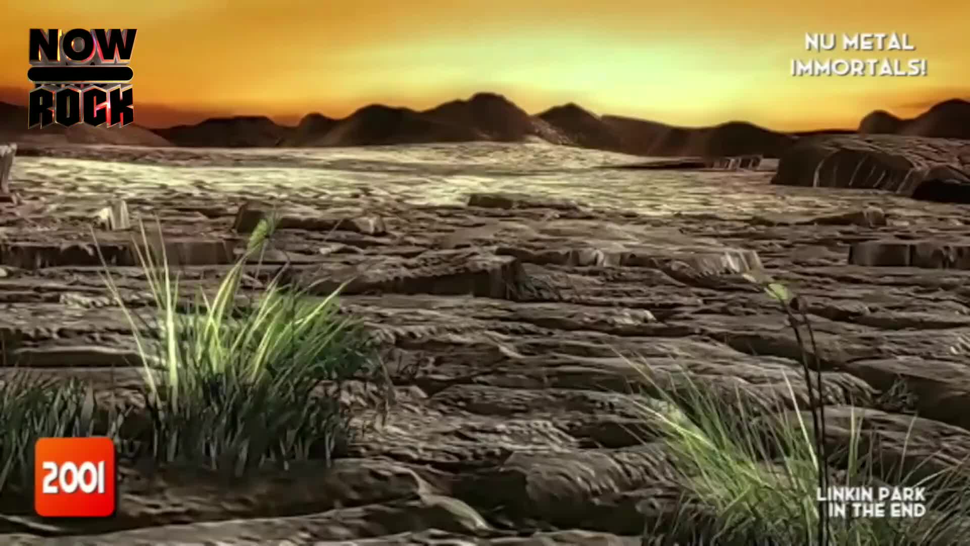 A rocky, barren landscape stretches out toward a hazy horizon. Patches of green grass sprout from the foreground, and the NOW Rock logo is visible in the cor...
