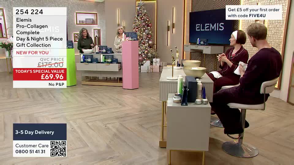 A woman and a man are seated at a table, both holding white cloths, as they appear to be part of a demonstration for a skincare product on QVC. Behind them, ...