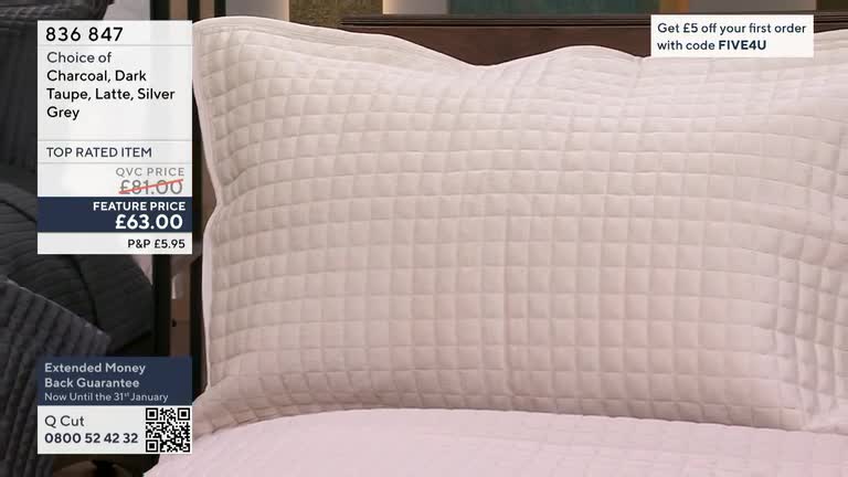 A large, quilted pillow sits on a bed, its neutral color illuminated by studio lights. The QVC price and feature price are displayed alongside the product, a...