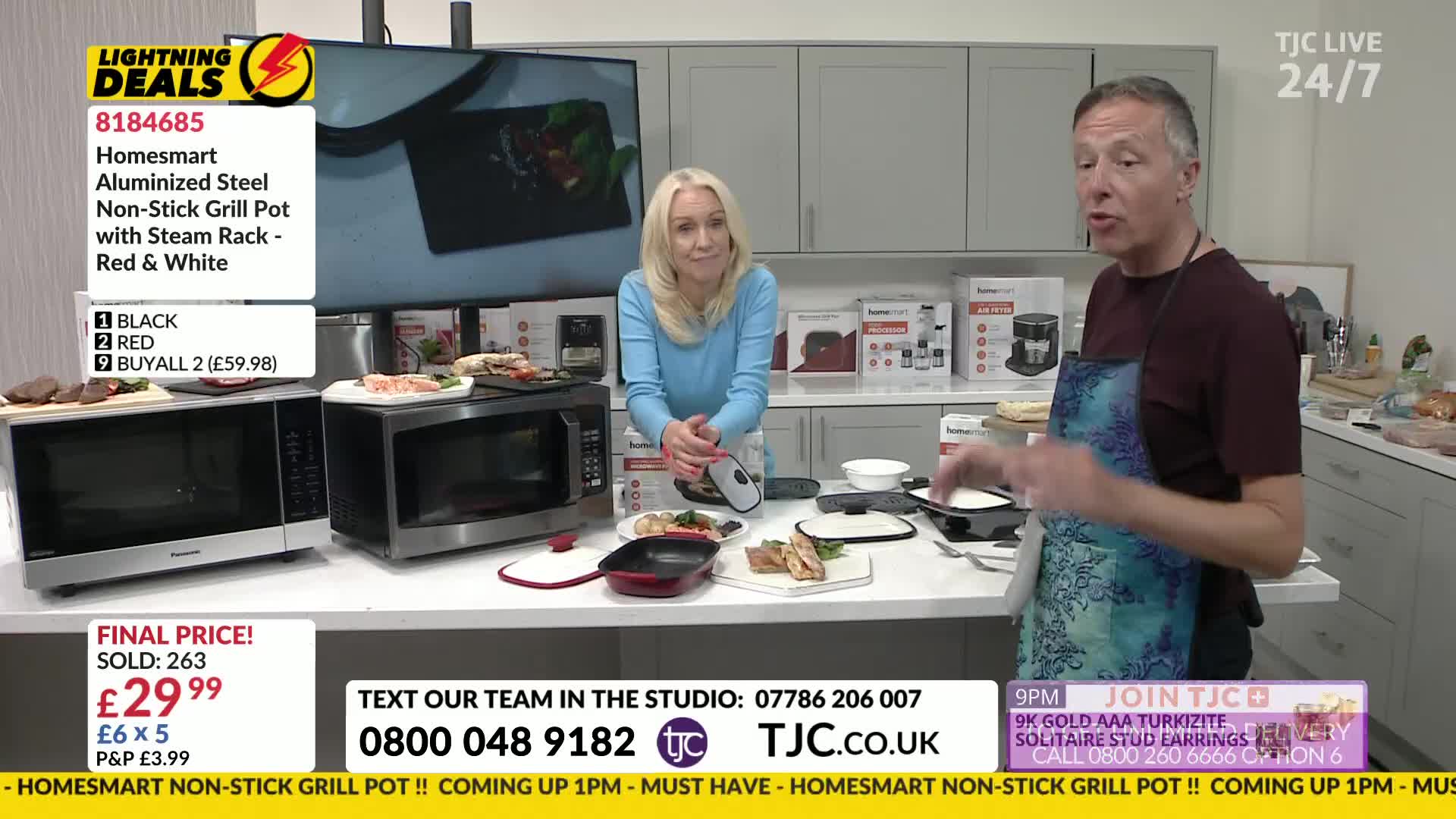 The man in the apron gestures towards a small grill, while the woman beside him smiles. On the counter, there's a microwave, some food, and a red grill pan, ...