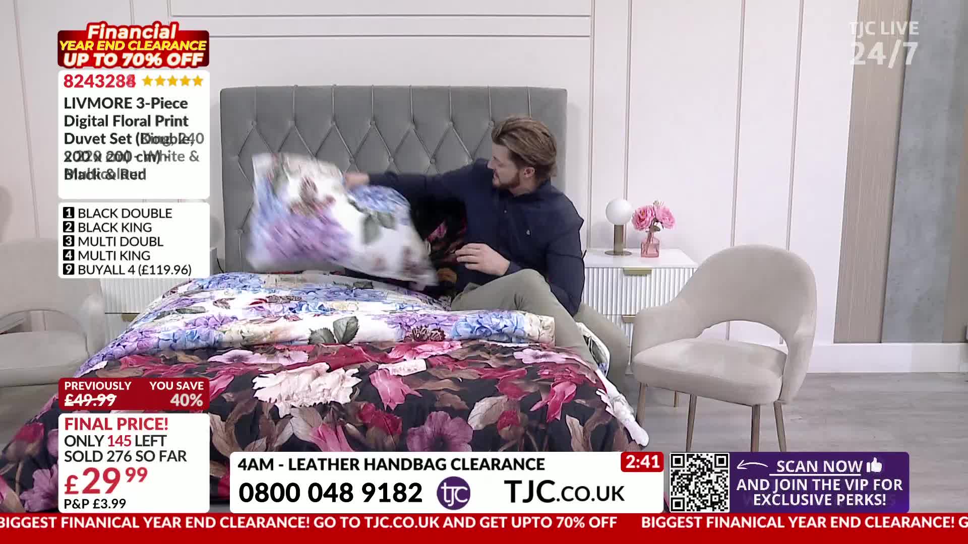 A man is arranging a floral-patterned duvet and pillow on a bed. The vibrant bedding features large blooms in shades of purple, pink, and white against a dar...