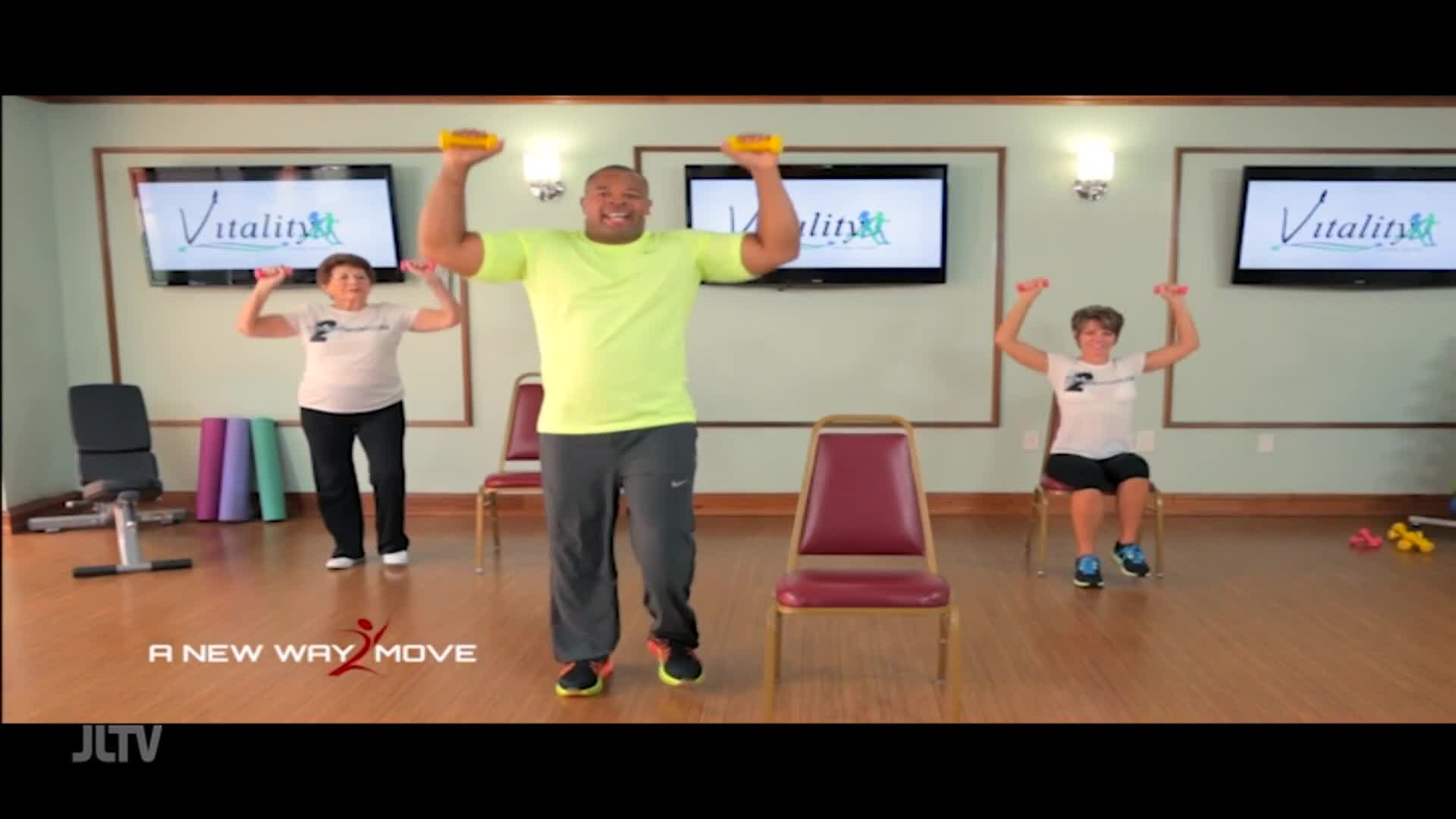 On Jewish Life Television, a man in a bright shirt leads a fitness class, lifting weights with two women. One woman stands, the other sits, both mirroring hi...