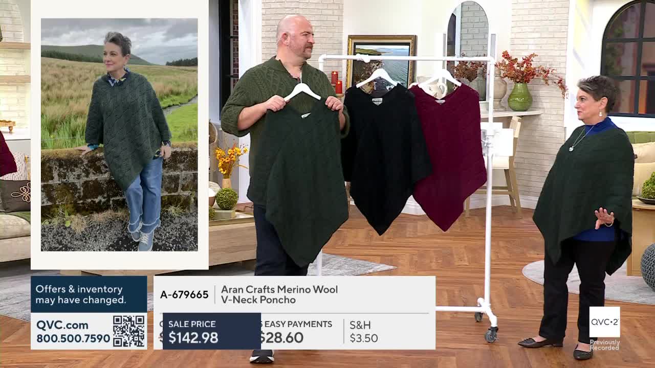 A man holds up a dark green poncho, showing its V-neck. Beside him, a woman stands wearing a similar poncho, gesturing toward a rack with other colors.