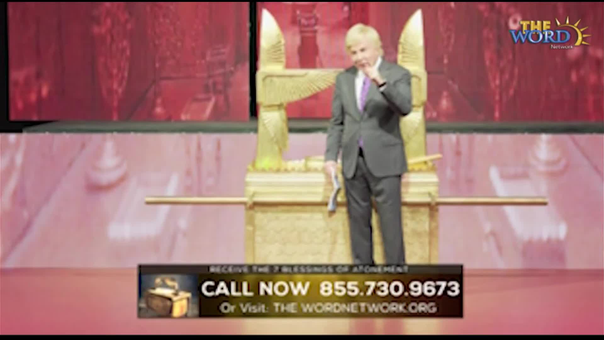 A man in a suit stands on a stage in front of a golden structure, holding a small paper. He touches his face thoughtfully, while a call-to-action banner sits...