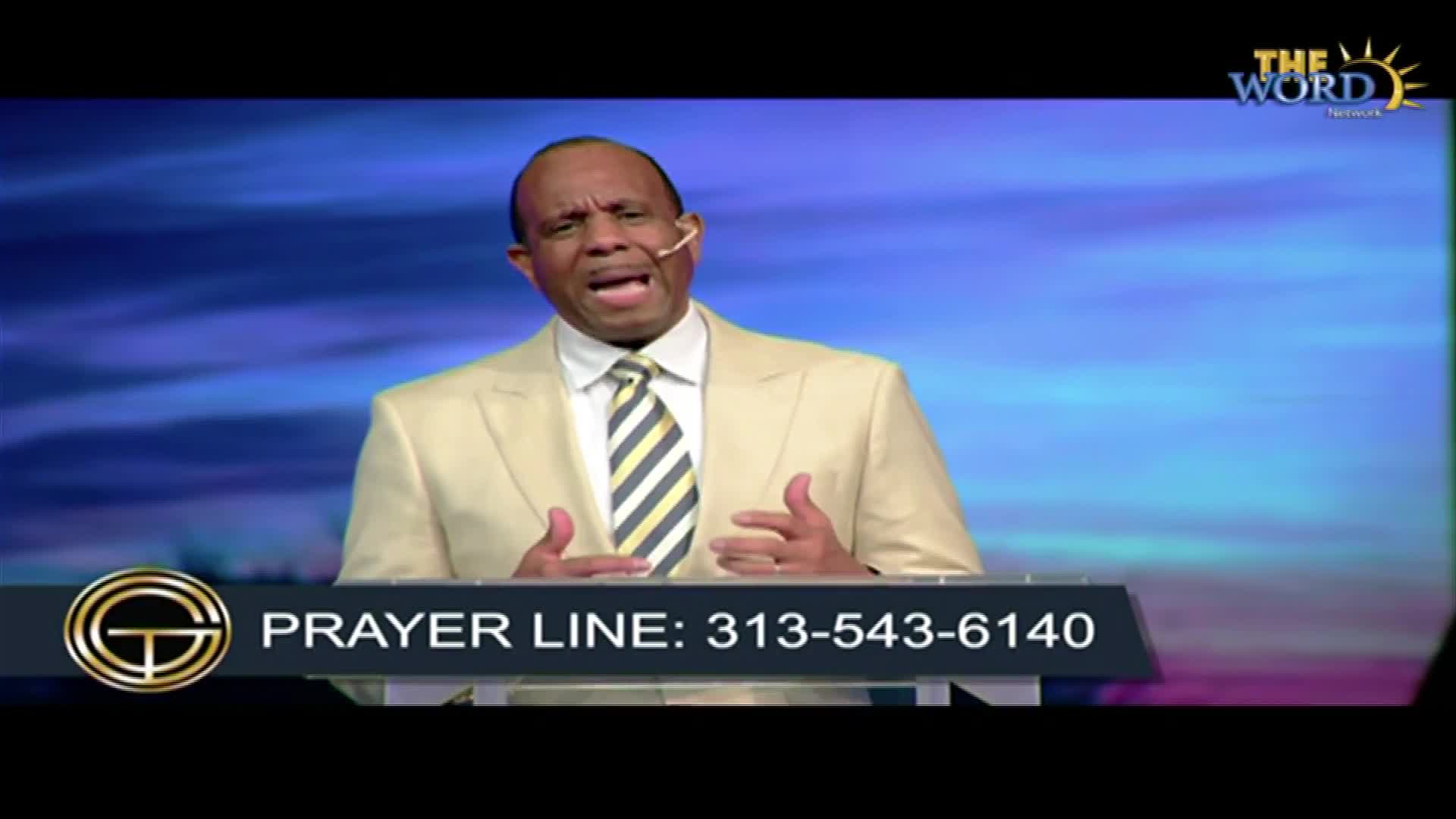A man in a light-colored suit speaks passionately, his hands gesturing as he addresses the camera. Below, a phone number for a prayer line is displayed on th...