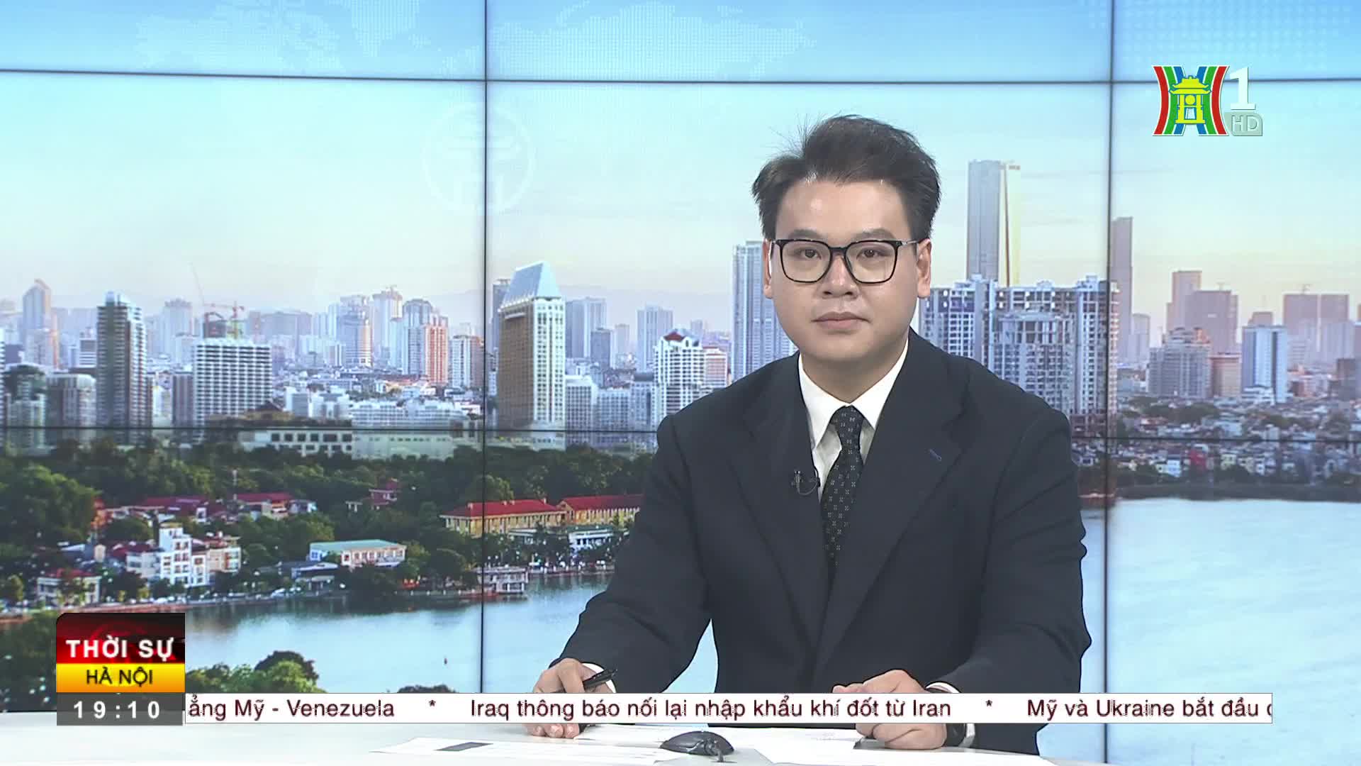 The news anchor, wearing a dark suit, sits behind a desk with a cityscape backdrop on HanoiTV1. The Thoi Su Ha Noi logo is visible in the lower left corner.