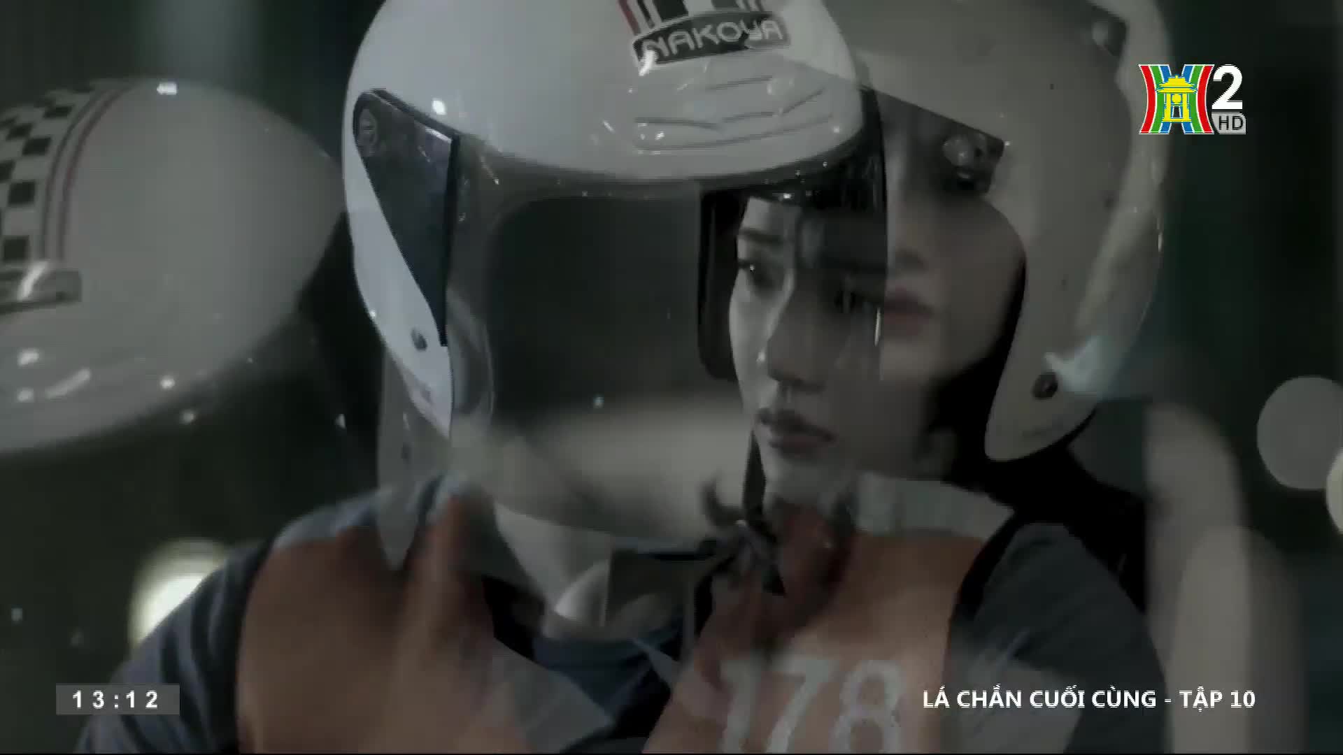 A woman in a white helmet, number 178 visible on her chest, stares ahead. The image, from HanoiTV2, is overlaid with a second helmet, creating a layered effect.