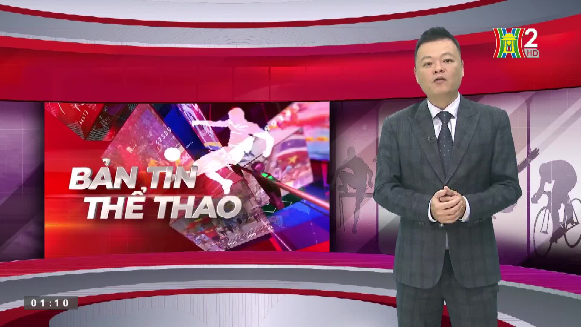 A man in a suit stands in front of a red and grey backdrop, speaking to the camera. The HanoiTV2 logo is visible in the top right corner, and the words "Bản ...